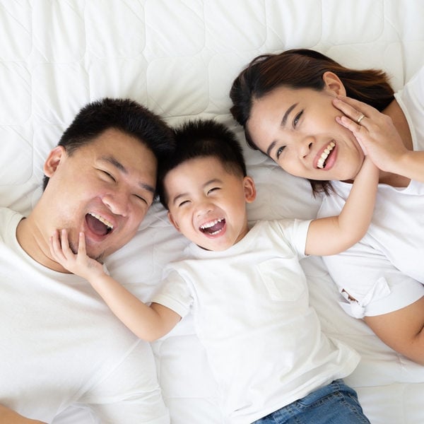 A family of three (father, child, mother) lying on a white bed, smiling and laughing together.” but only one sentence per item